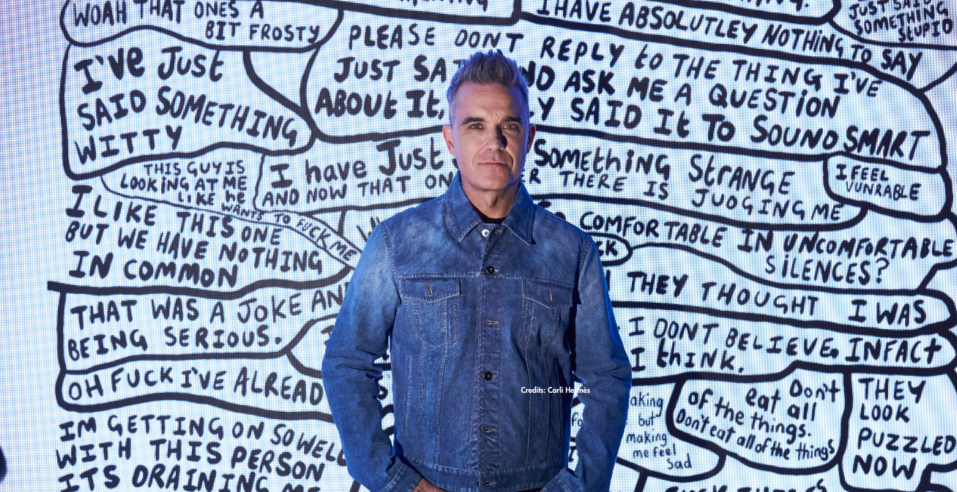 Robbie Williams in front of handwritten black-and-white text art, part of his exhibition at Moco Museum Amsterdam.